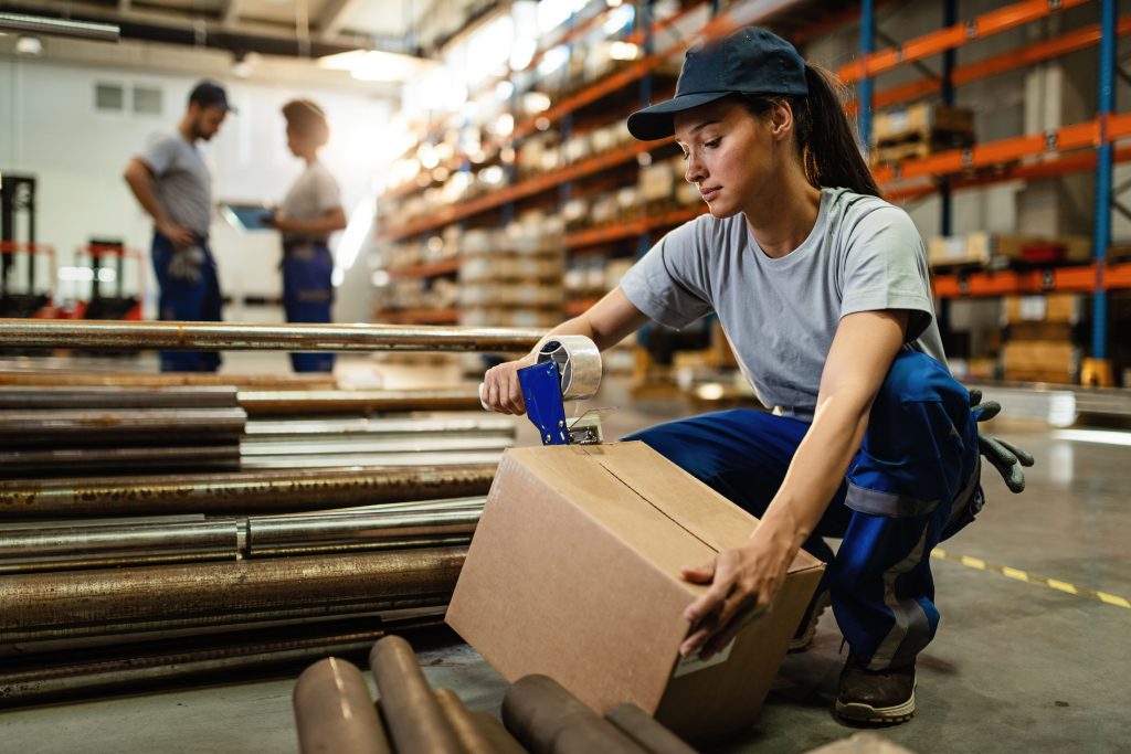 female-warehouse-worker-taping-cardboard-box-with-tape-dispenser-before-shipment (1)